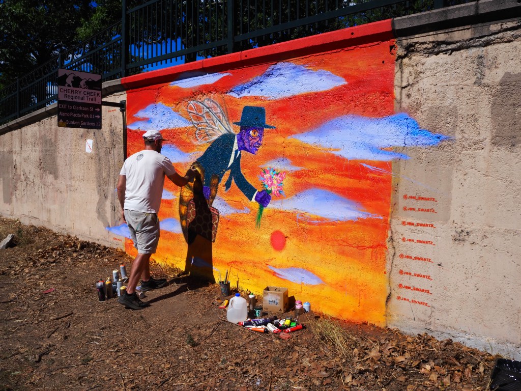 A man paints a colorful mural of a business man/bee