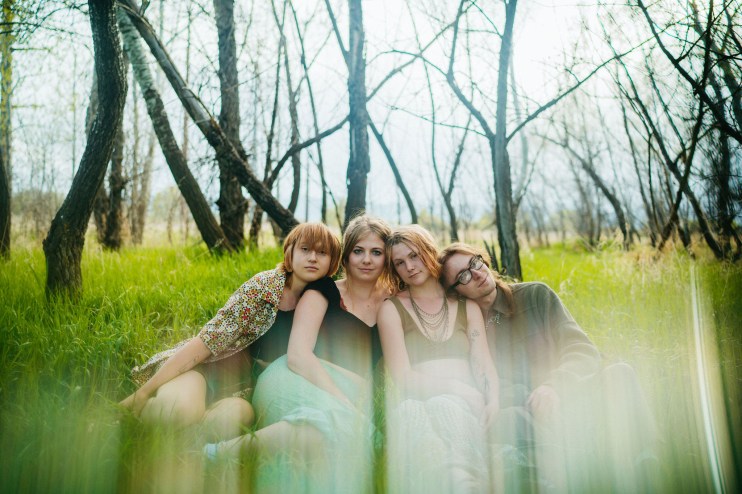 Four women sitting in grass surrounded by trees.