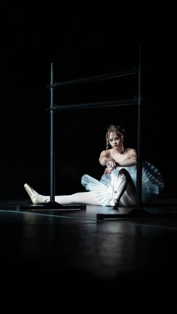A ballerina sits on the floor.