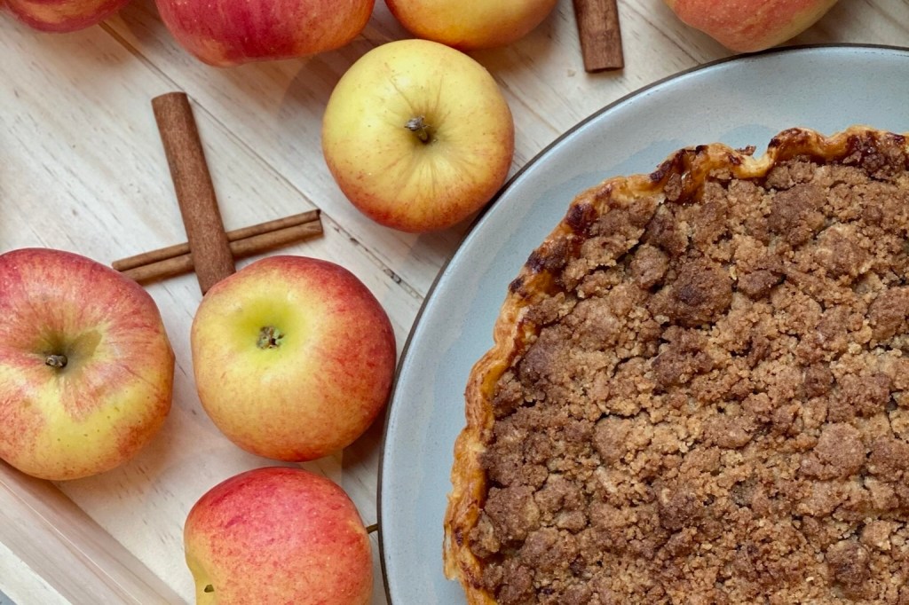 Fresh apples and cinnamon sticks displayed next to a whole apple pie from Tavernetta