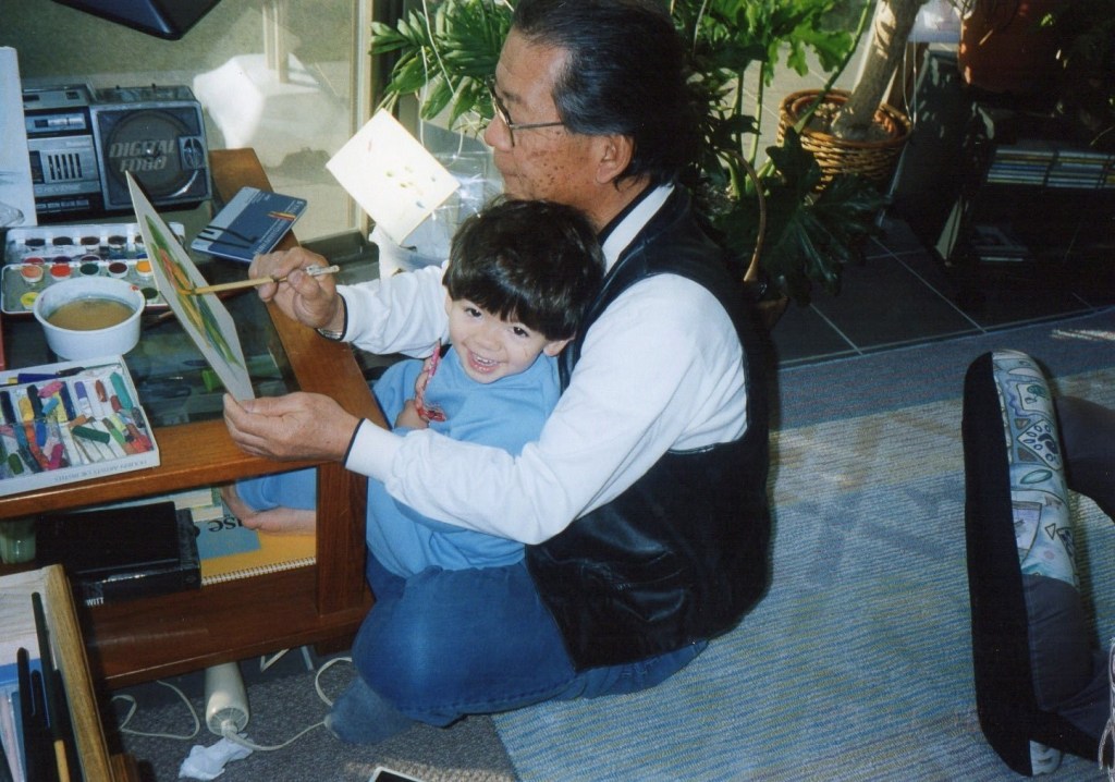 Young Joshua Ryuju sits on his grandfather's lap.