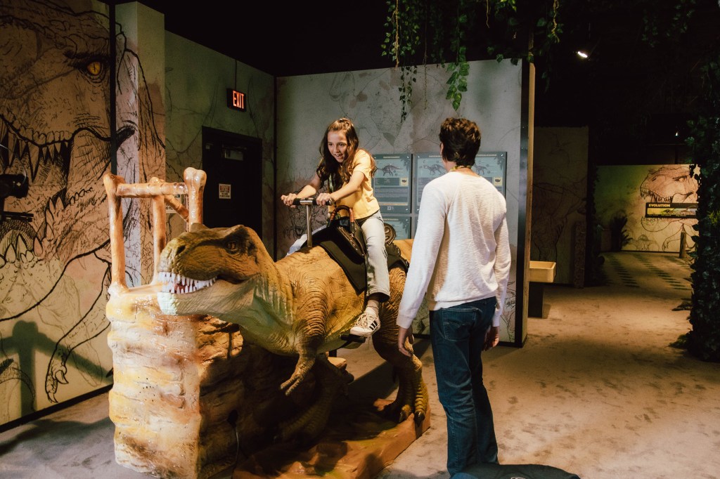 A kid rides a dinosaur.