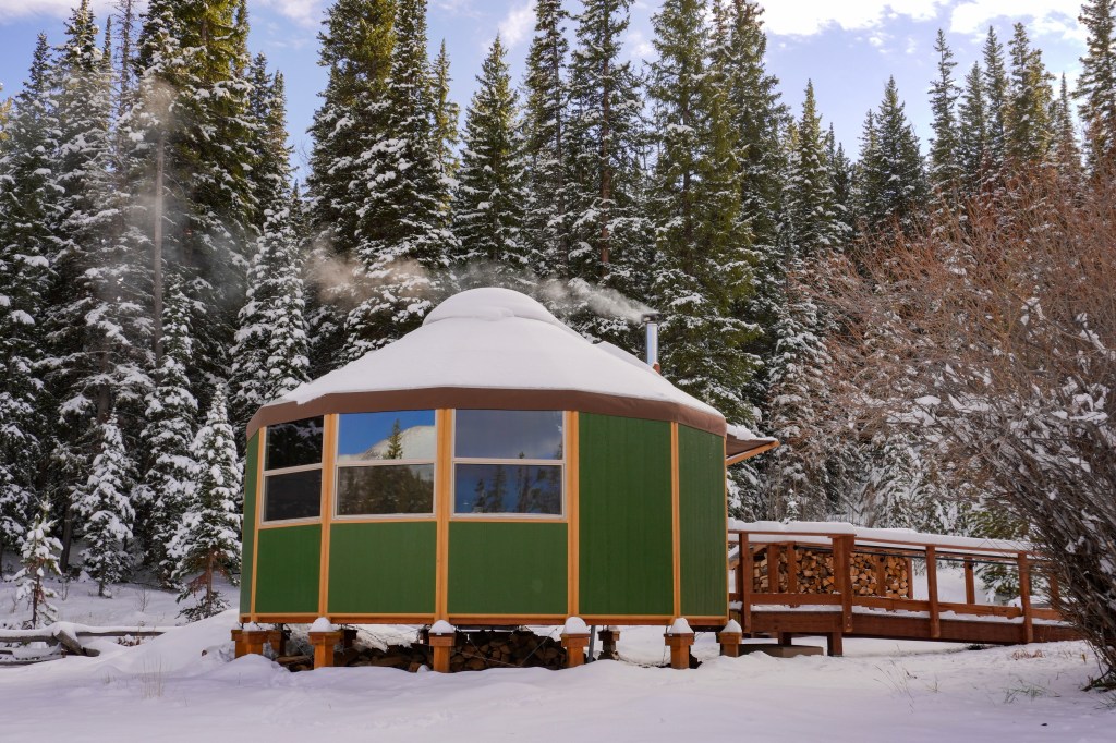 A green hut from Yonder Yurts backdropped by an evergreen forest