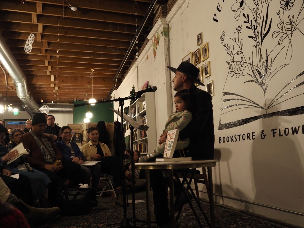 A man holds a child while doing a poetry reading