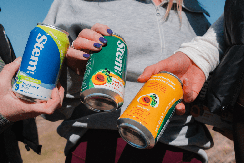 A close-up of three people holding cans of Stem Zero flavors