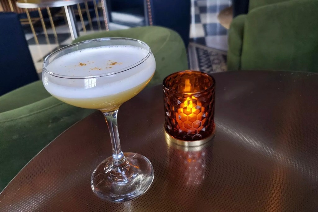 A coupe glass of the Goldfinch's eponymous signature cocktail, featuring egg white and gold dust