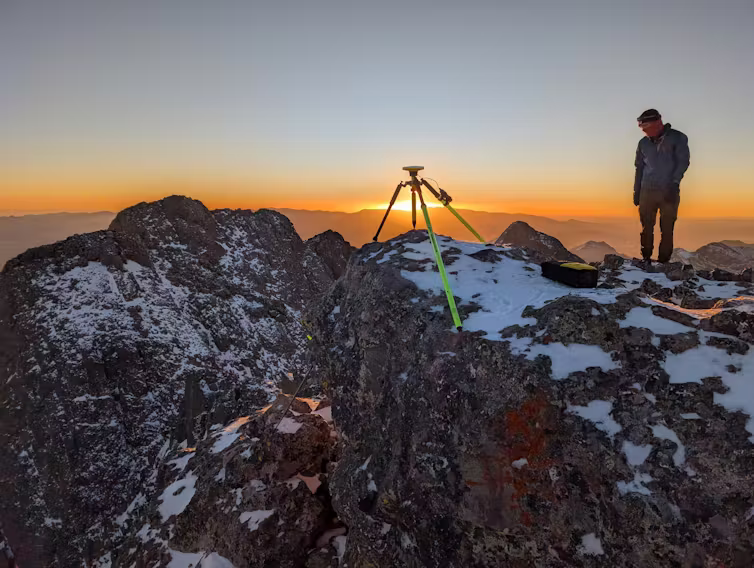 man measures 14er mountain summit during sunset
