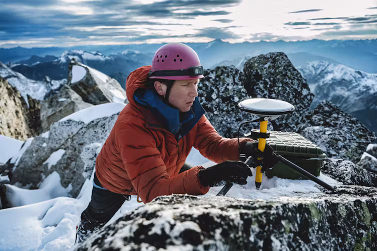 man sets up GPS device on snowy mountain top