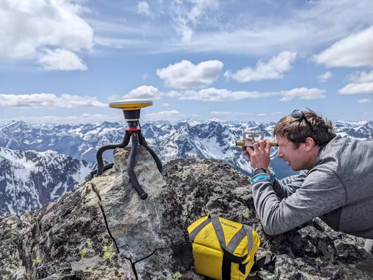man looks through binoculars on mountain peak