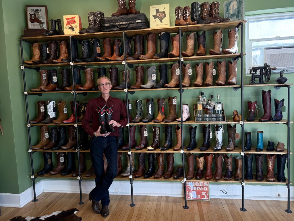 A man stands in front of shelves of cowboy boots