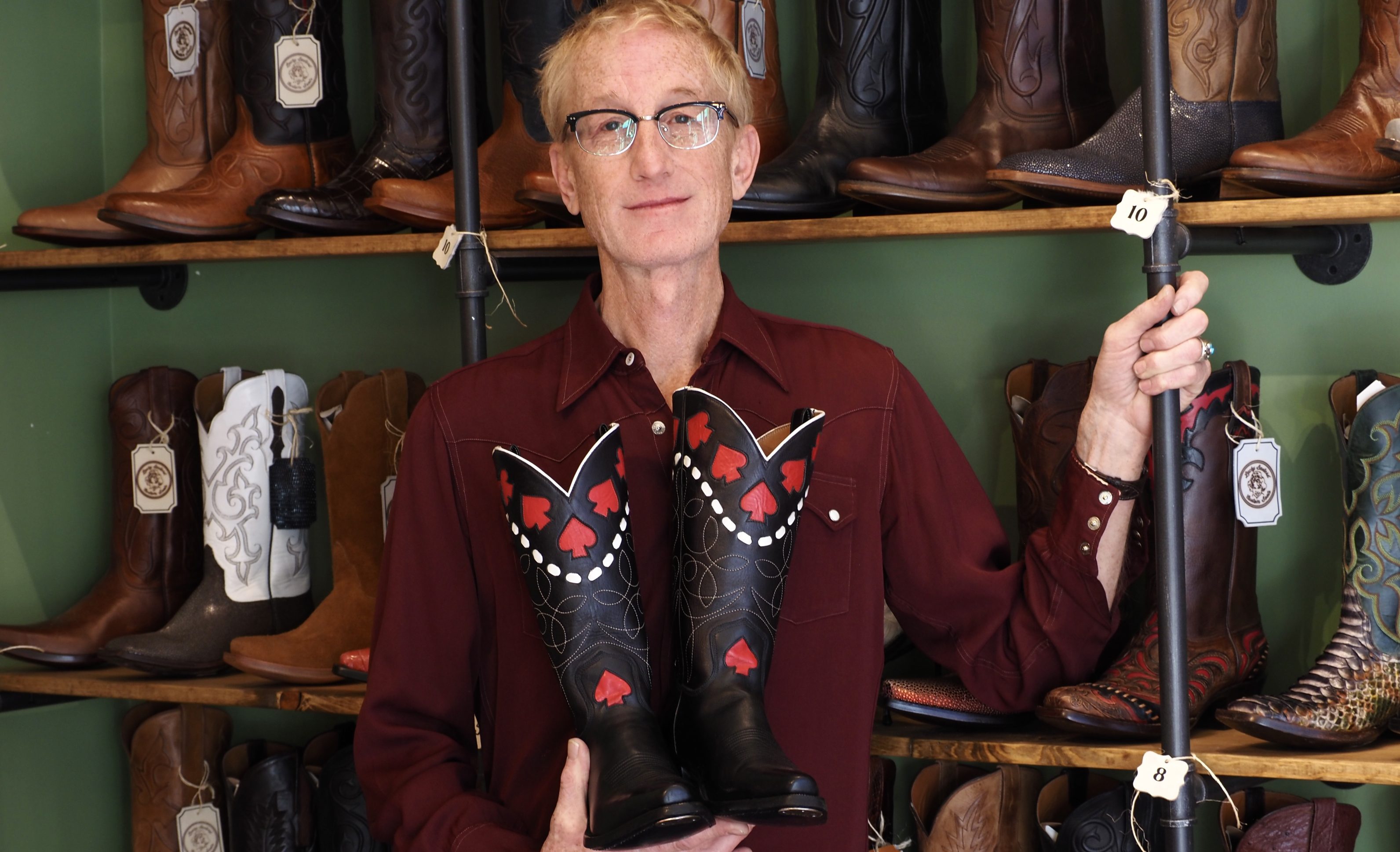 A man holds a pair of cowboy boots with red spades on them