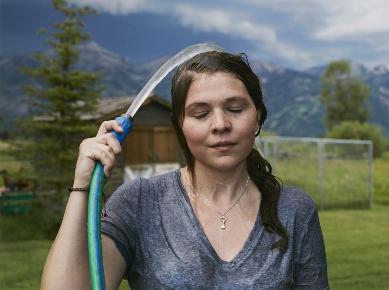 A photograph of a woman spraying herself with a hose