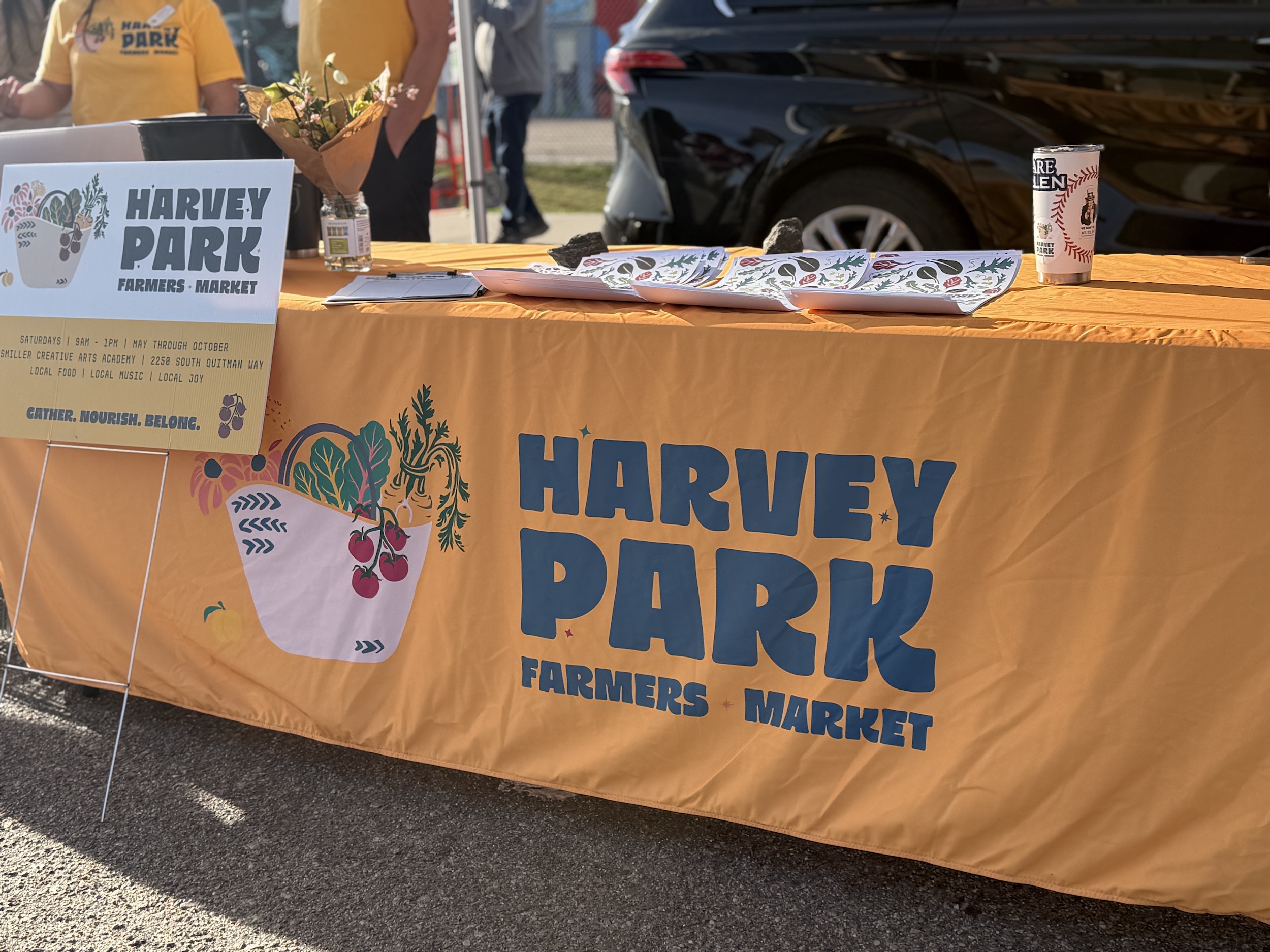 table with a "Harvey Park Farmers Market" branded orange tablecloth