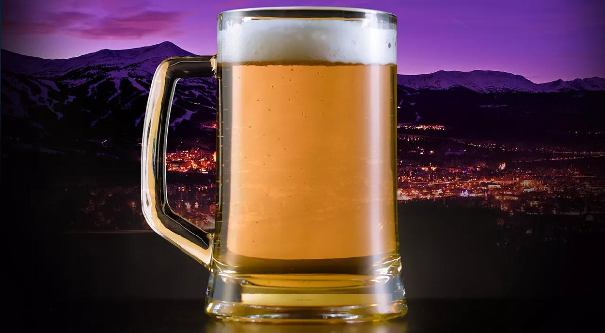 a mug of beer against the backdrop of Denver's skyline at night.
