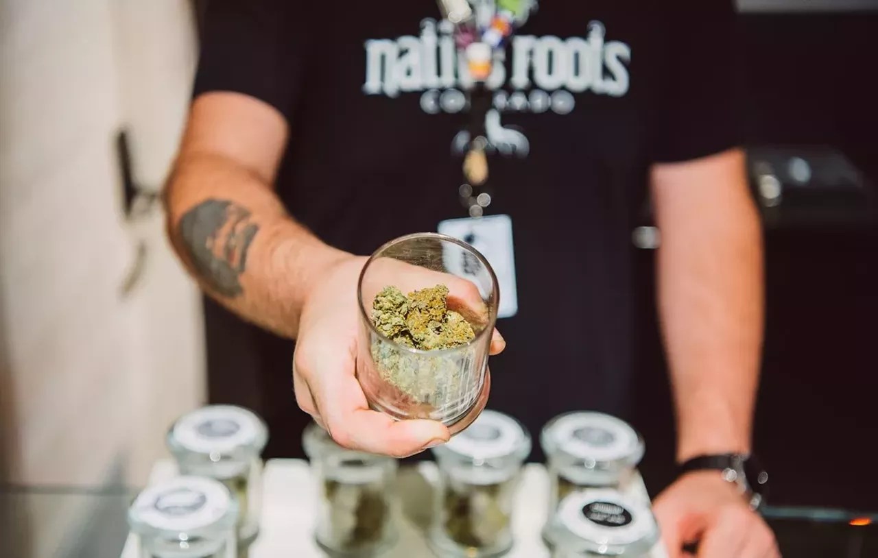 a dispensary budtender holds a display jar of cannabis open in front of the camera