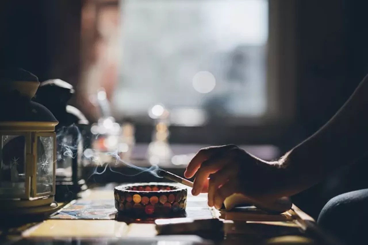A person holds a smoldering joint over an ashtray.