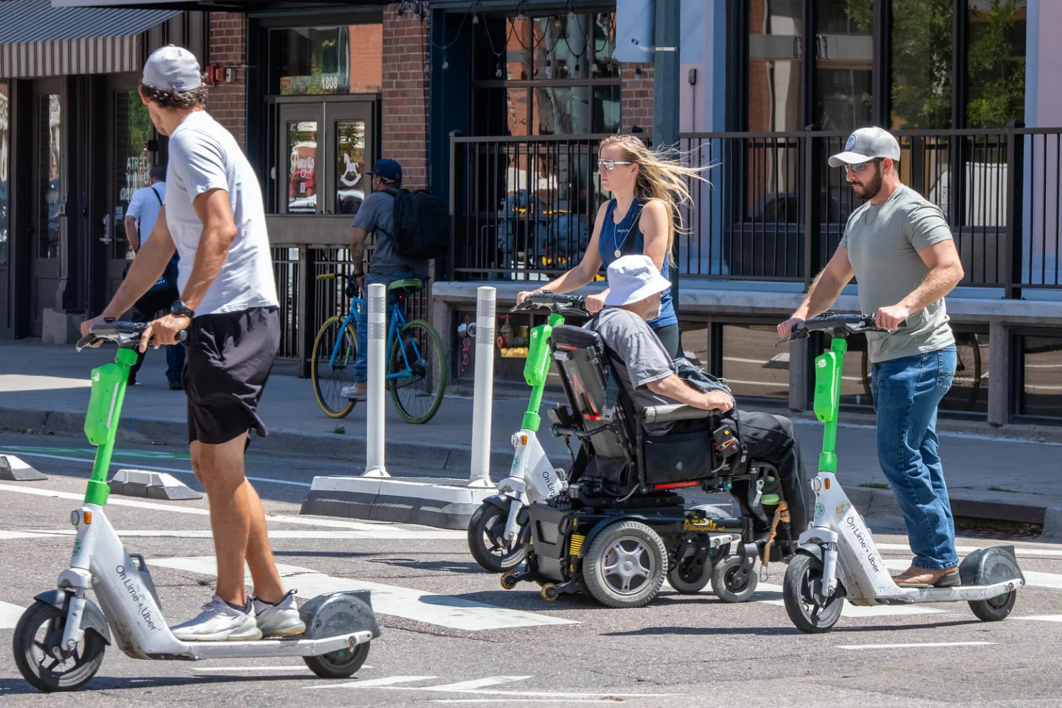 e-scooter riders and a man in a wheelchair cross the street in downtown Denver