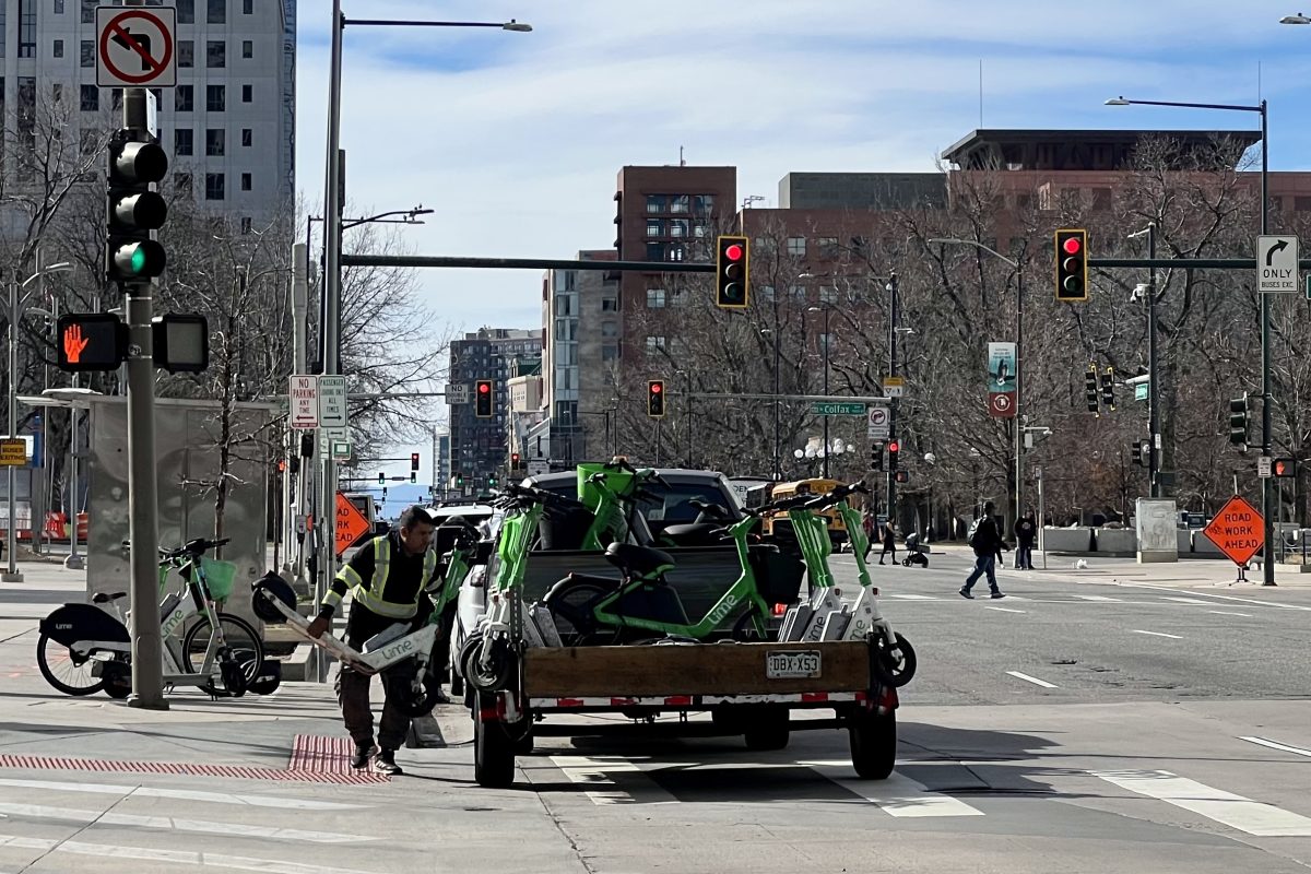 A man loads numerous Lime e-scooters into a truck in downtown Denver.