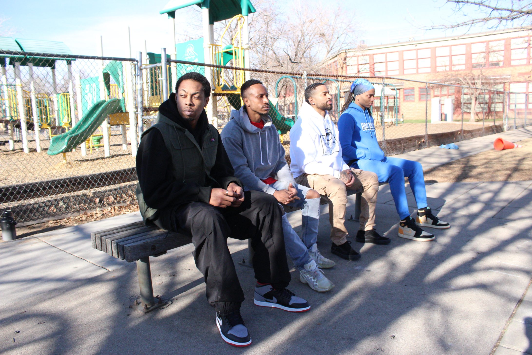 Four black men sit on a park bench