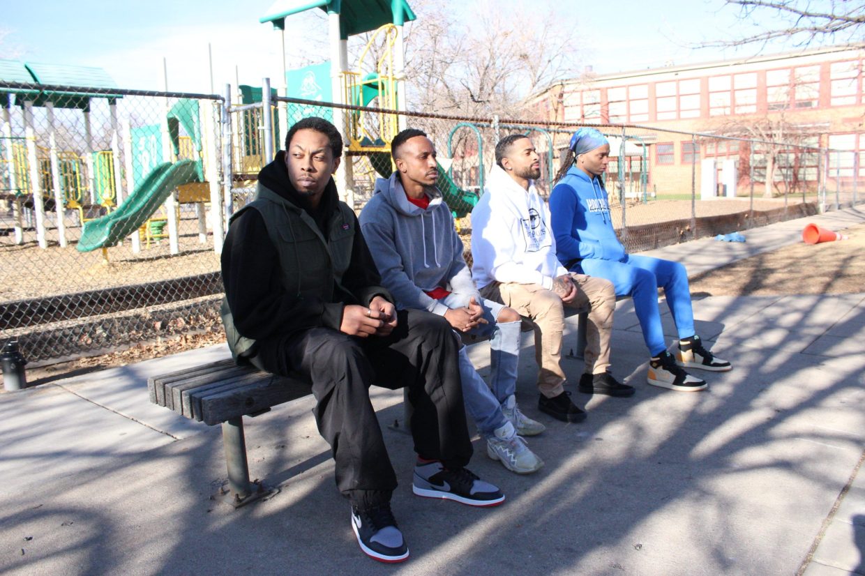Four black men sit on a park bench