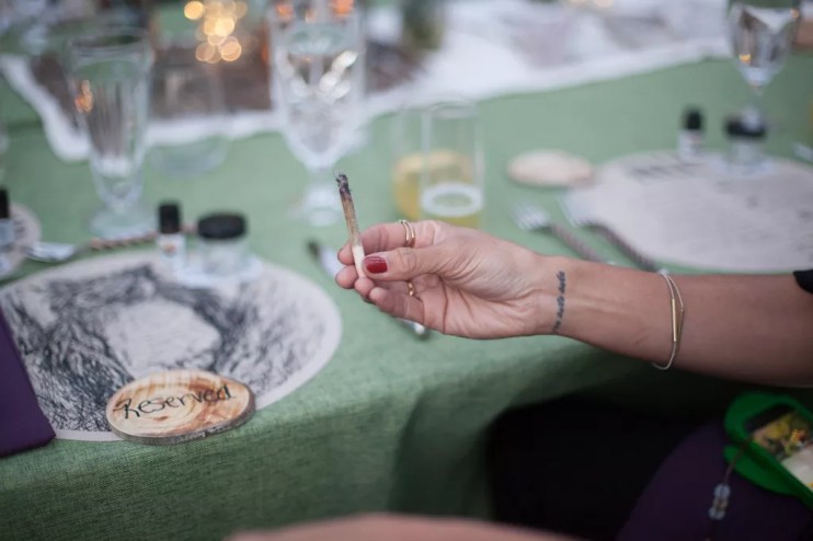 A woman holds a marijauna joint at dinner