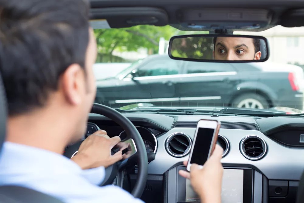 man driving car holding cell phone