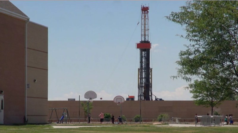 In the foreground, are basketball hoops. In the background, a fracking rig.