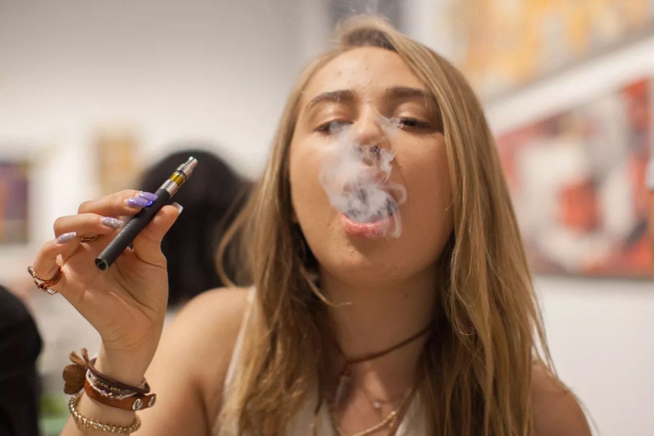 Young woman blows smoke while vaping.