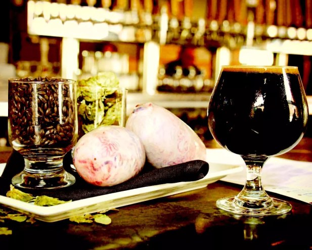 a glass of dark beer next to two bull testicles