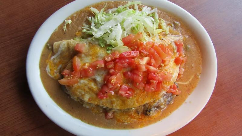 green chile and cheese on top of a tortilla on a plate with lettuce and tomatoes