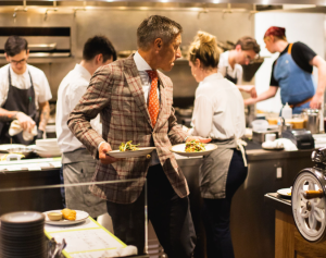 a man in a suit holding plates in a kitchen