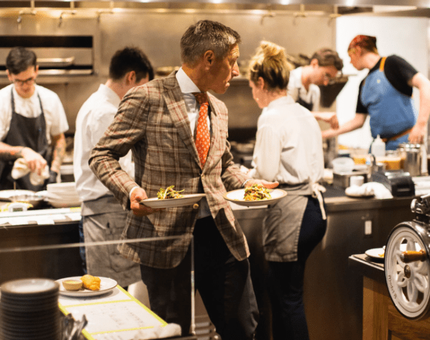 a man in a suit holding plates in a kitchen
