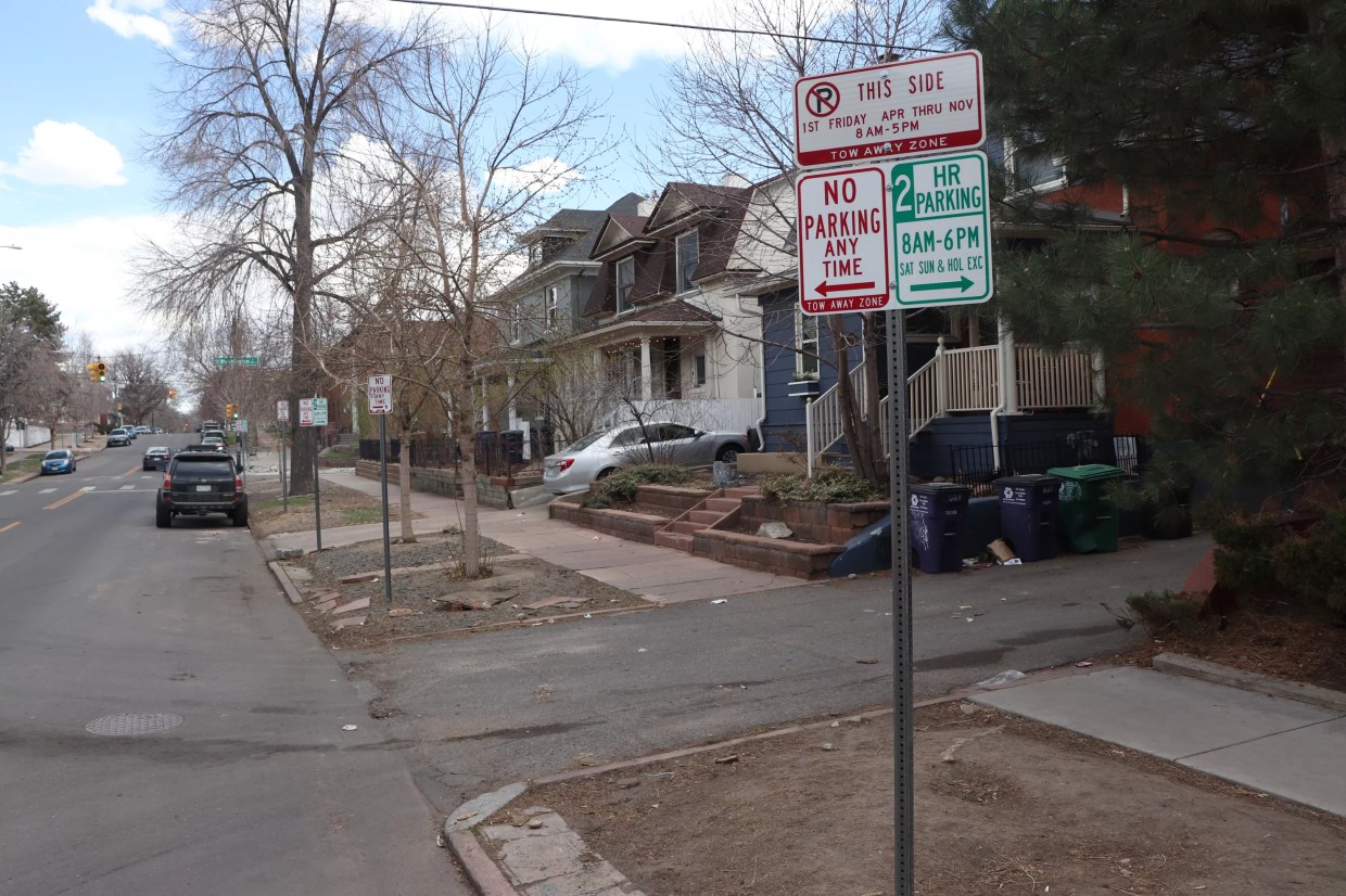 A parking regulations sign graces the corner of a city street lined with single-family homes.