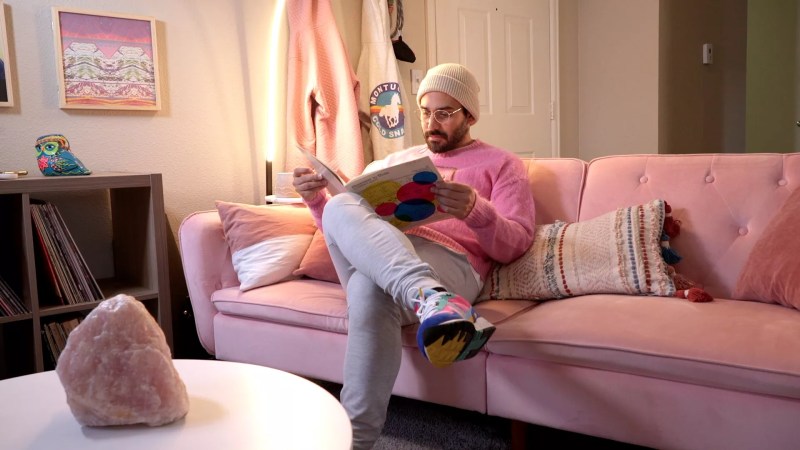man in pink shirt reads book on pink sofa