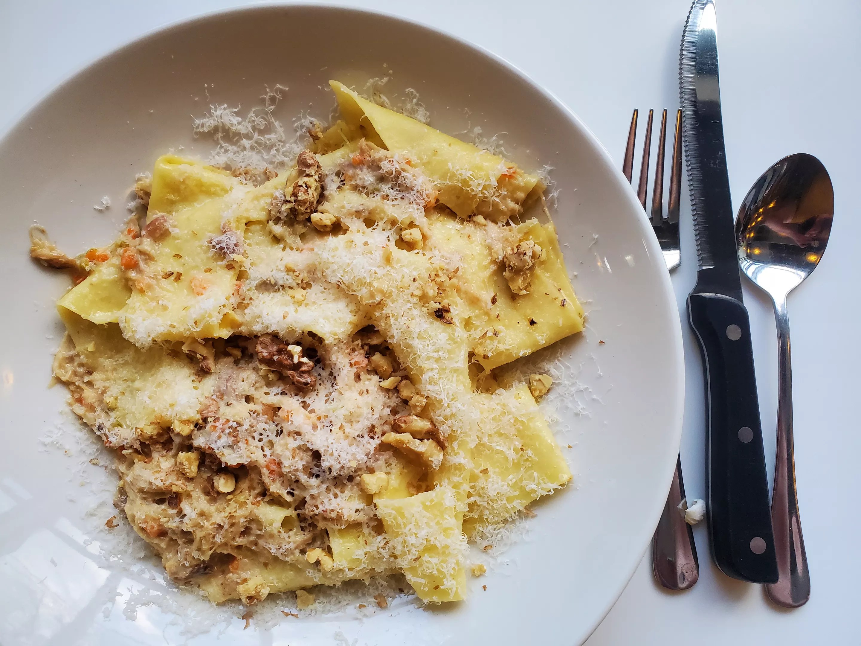 a plate of pappardelle pasta nest to a fork and knife.