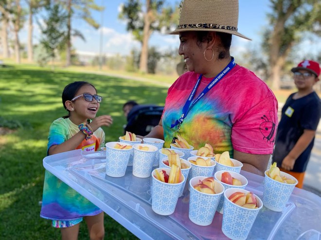 a woman holding a tray of apple slices in cups next to a child smiling