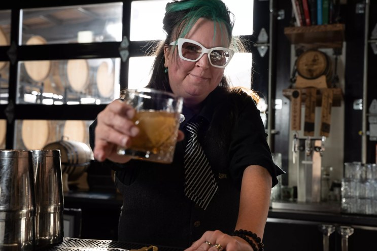a woman with teal hair and a black and white striped ties holding a cocktail