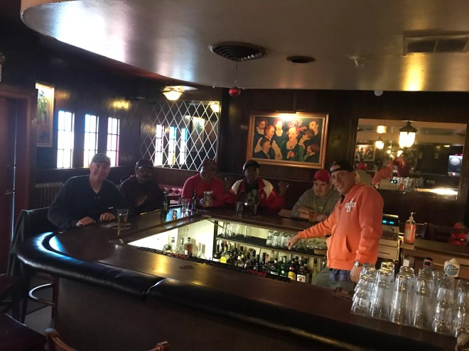 a man in an orange hoodie stands behind a bar where patrons are seated