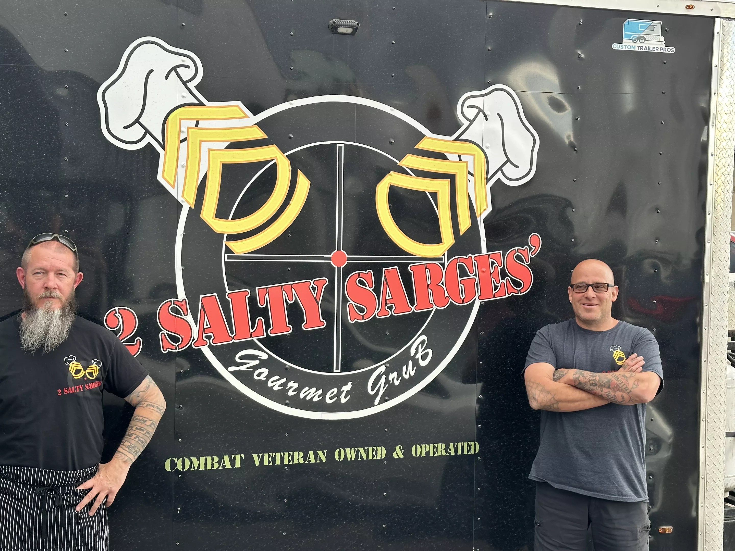 two men standing in front of a black food truck