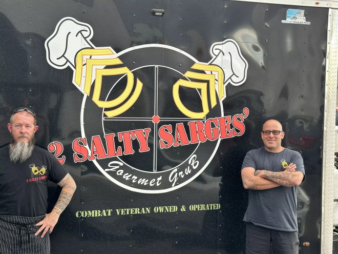 two men standing in front of a black food truck