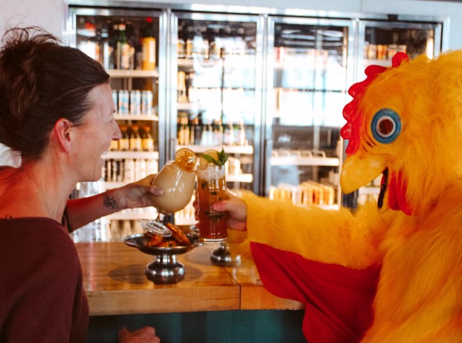 woman talks to person in chicken suit while drinking