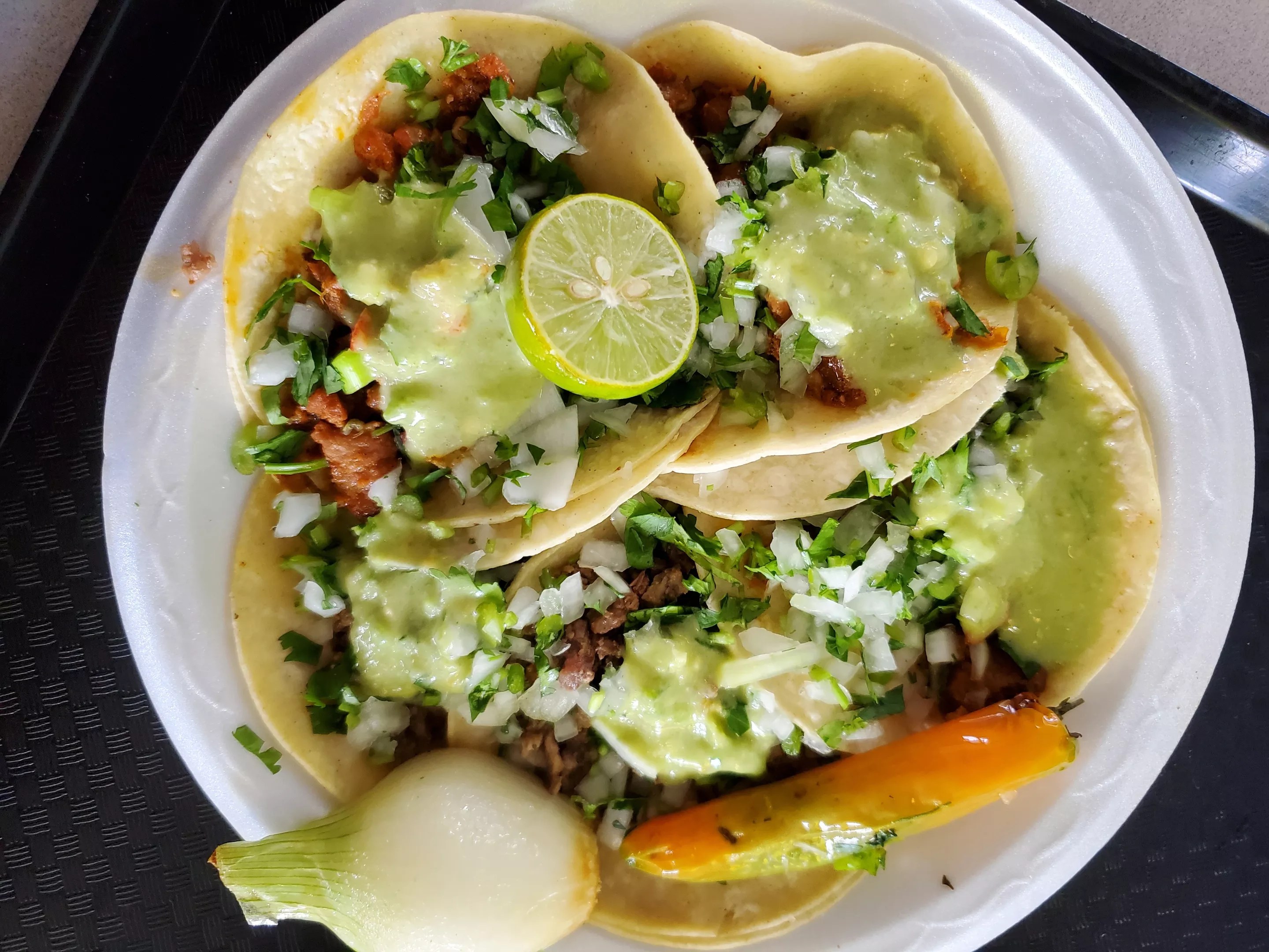 a plat of tacos topped with onions, cilantro and green salsa