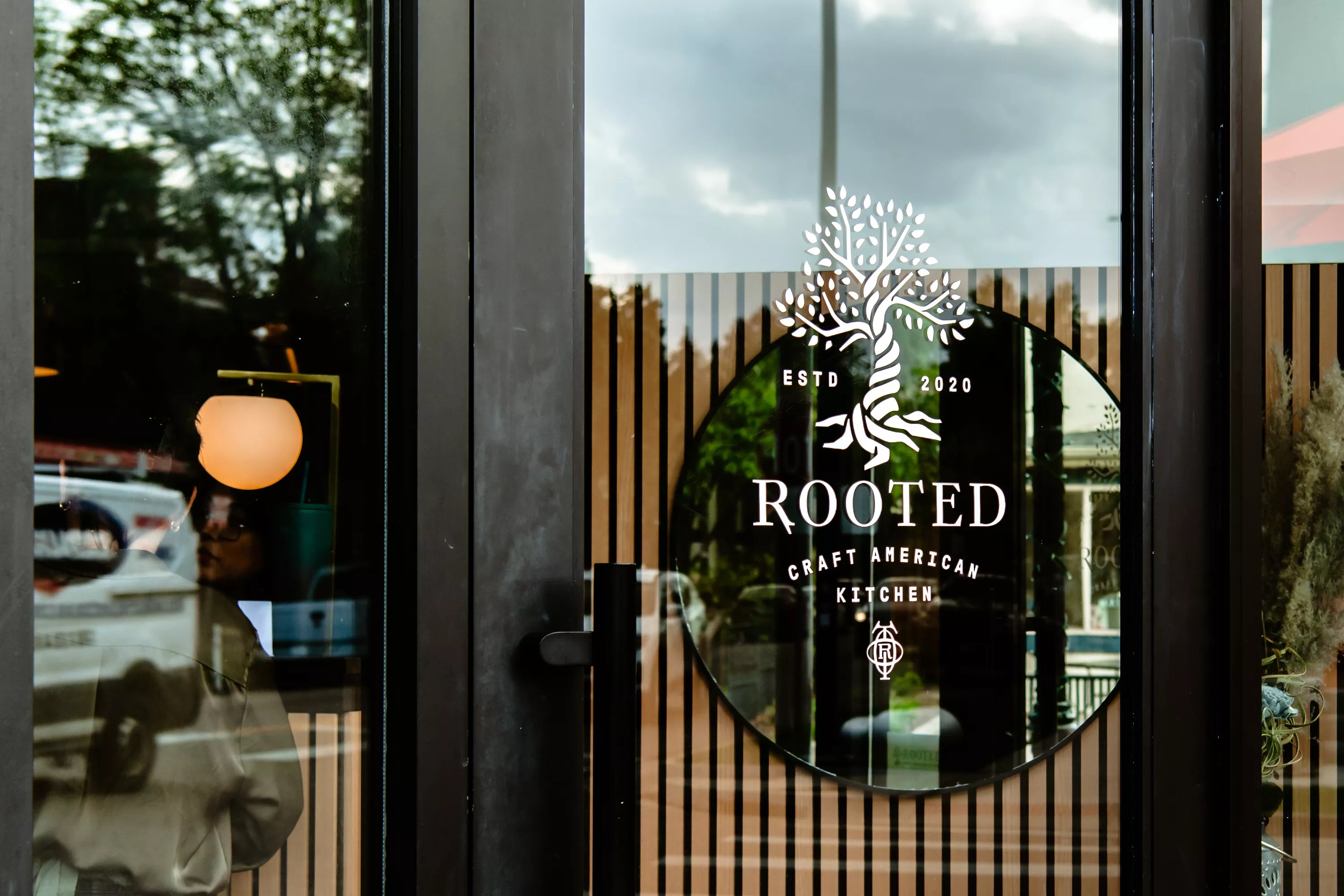 a black sign that says "rooted" behind a glass door