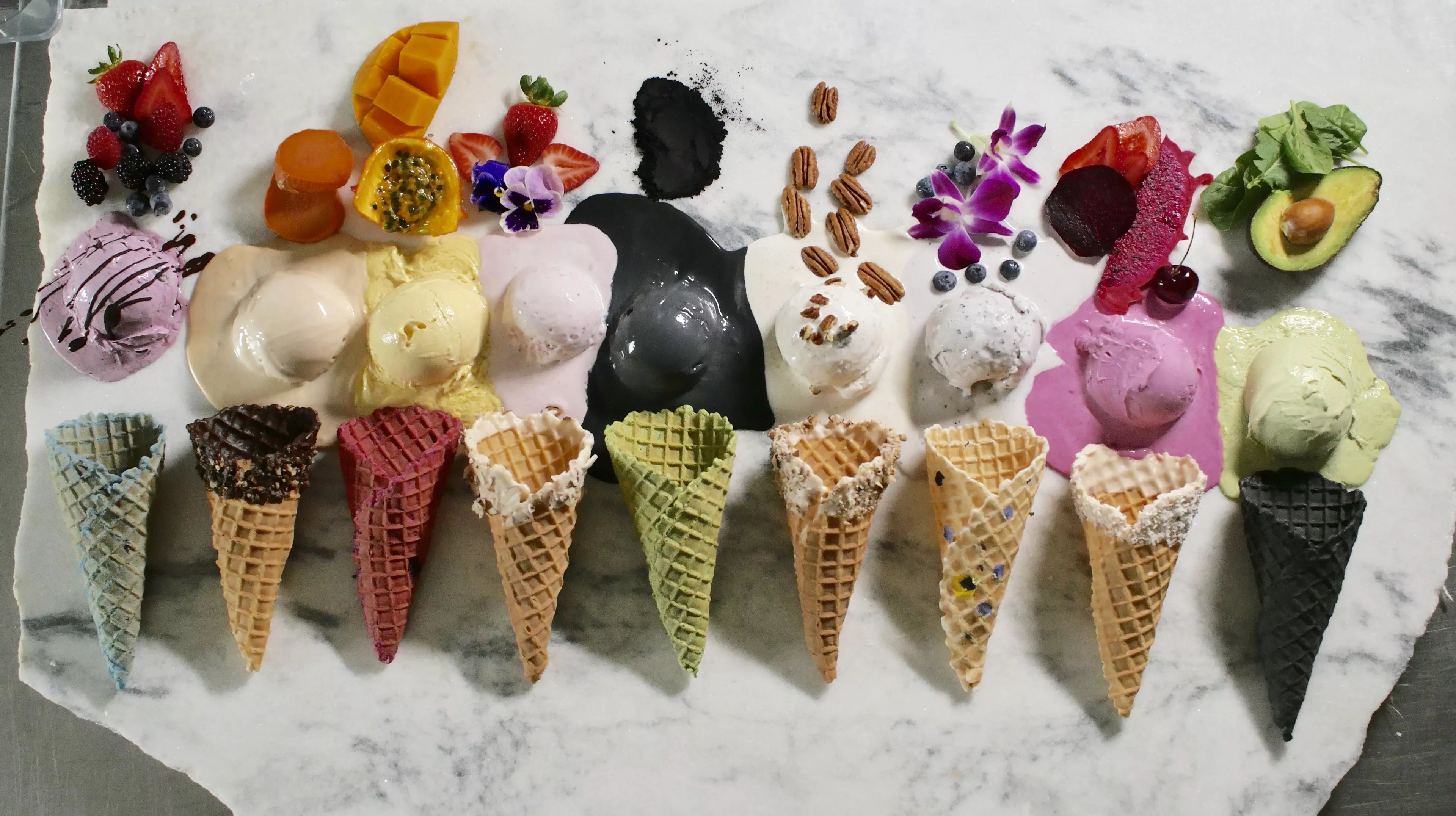 a row of ice cream cones and scoops of ice cream with various toppings laying on a marble background.