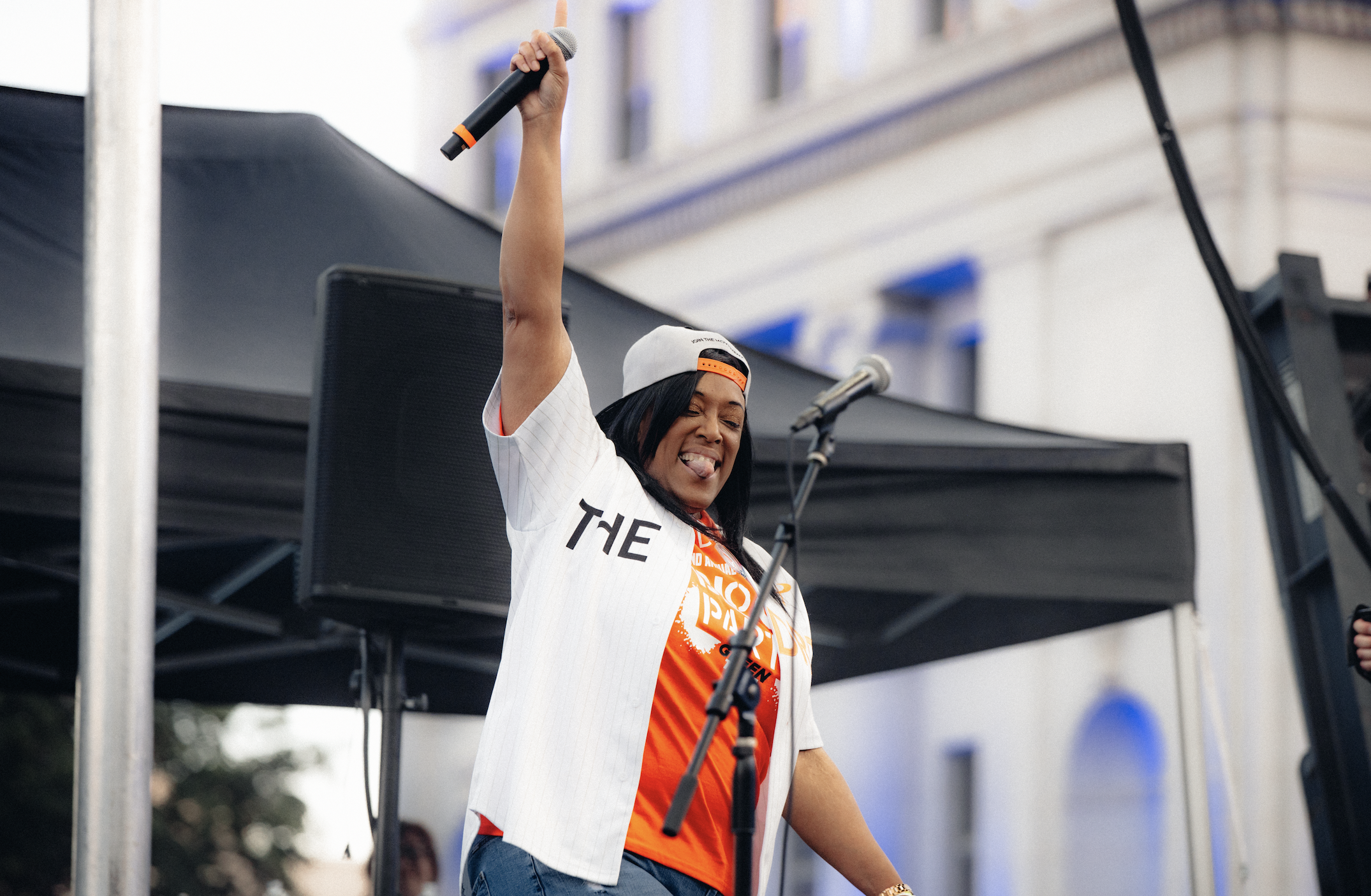 woman holds up a microphone on stage and smiles