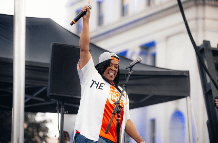 woman holds up a microphone on stage and smiles