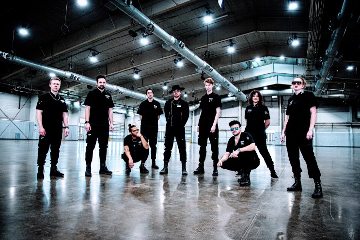 nine bandmates stand in an empty room