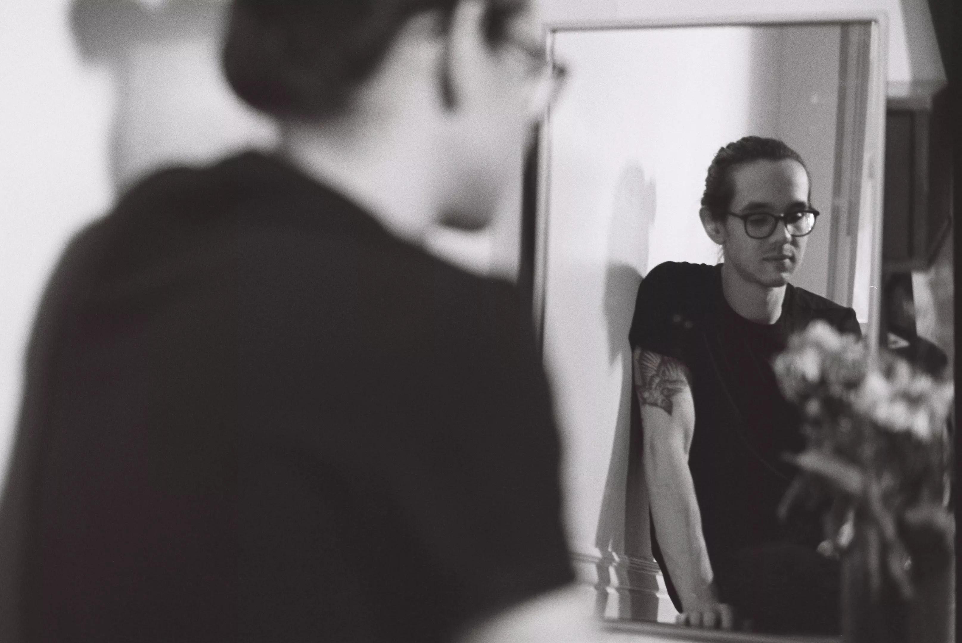 man with glasses and black t-shirt looks in mirror.
