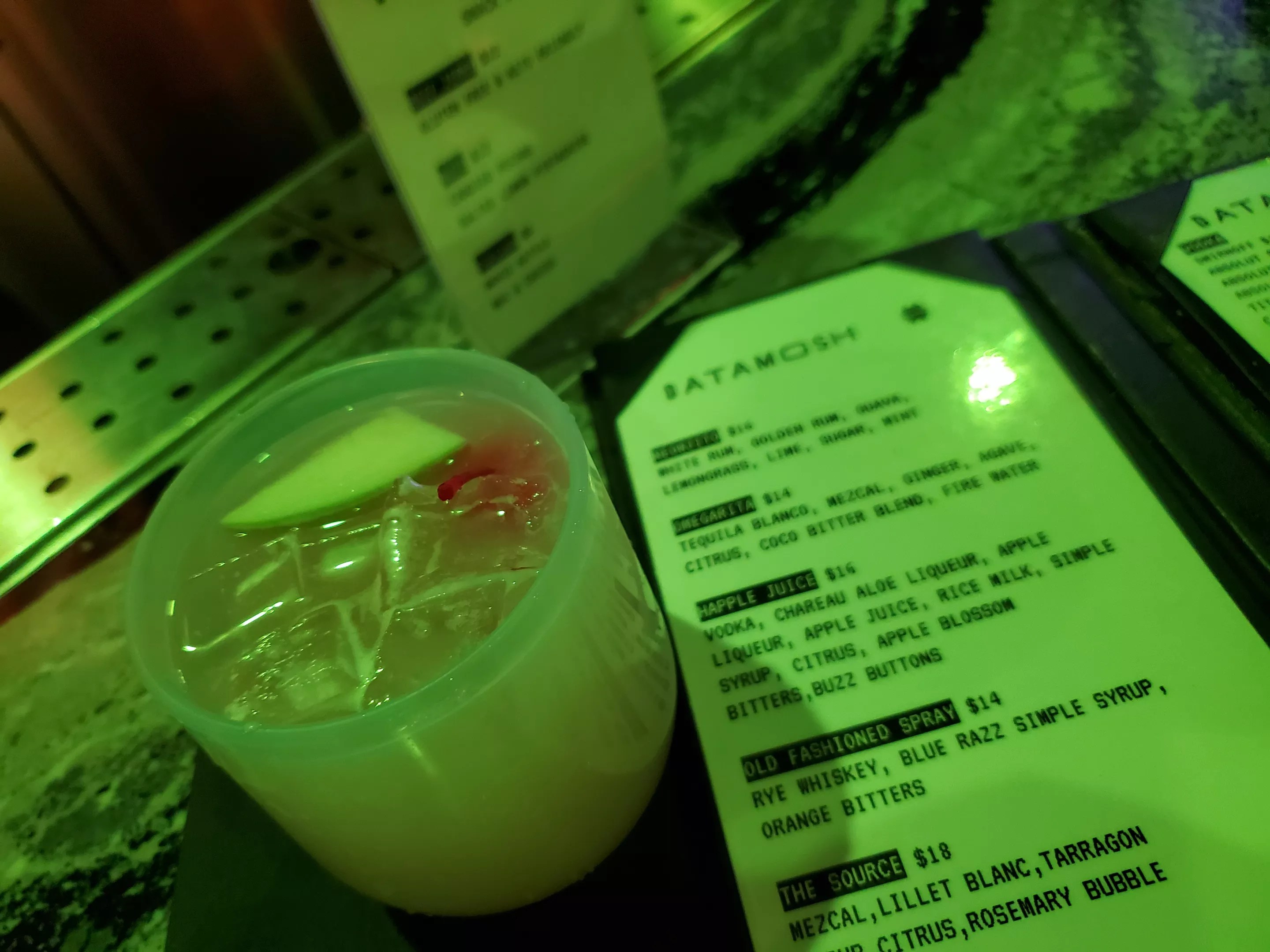 a cocktail  next to a menu in green light
