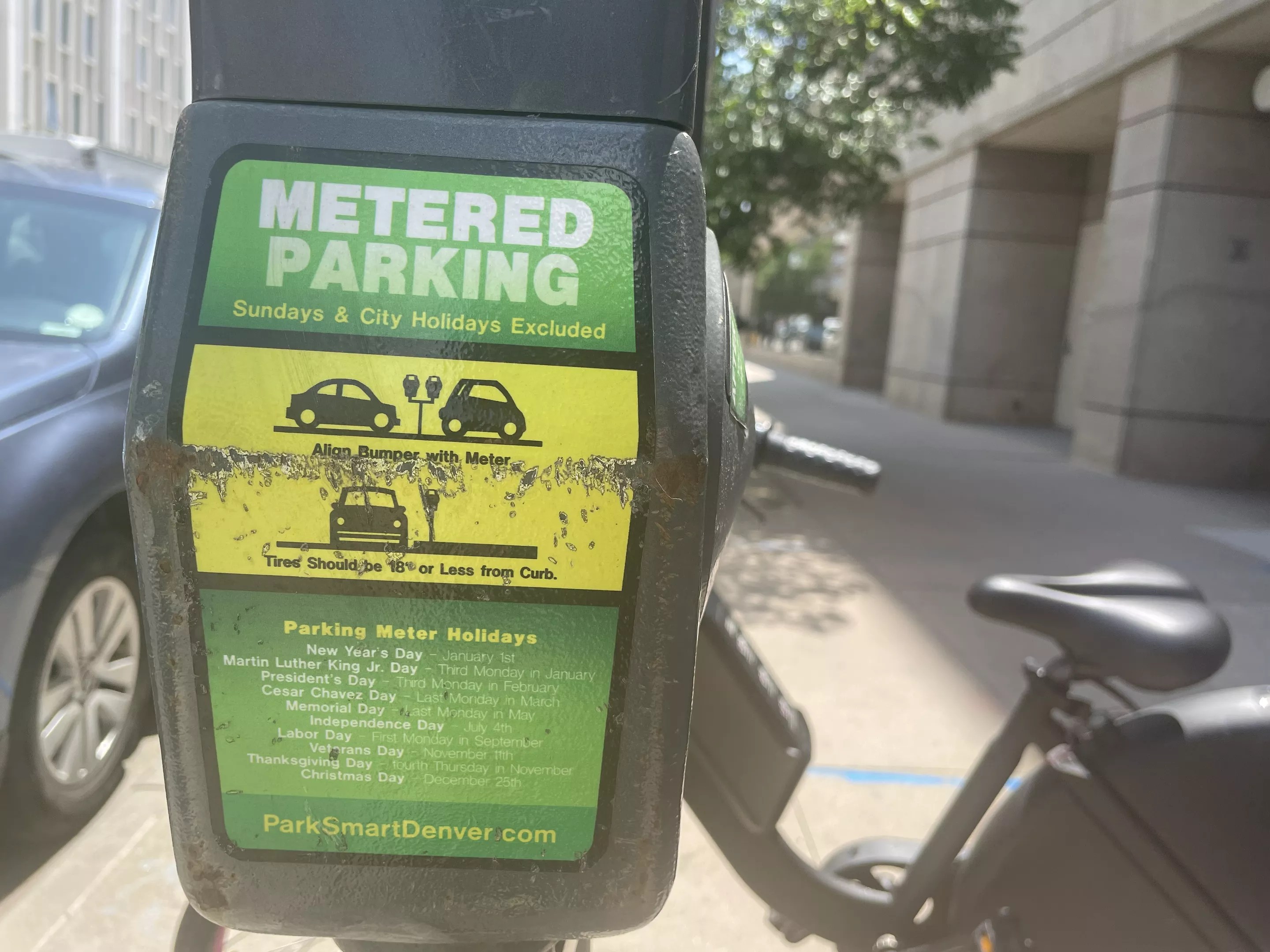 A green and yellow sticker on a parking meter shares information about parking in Denver.